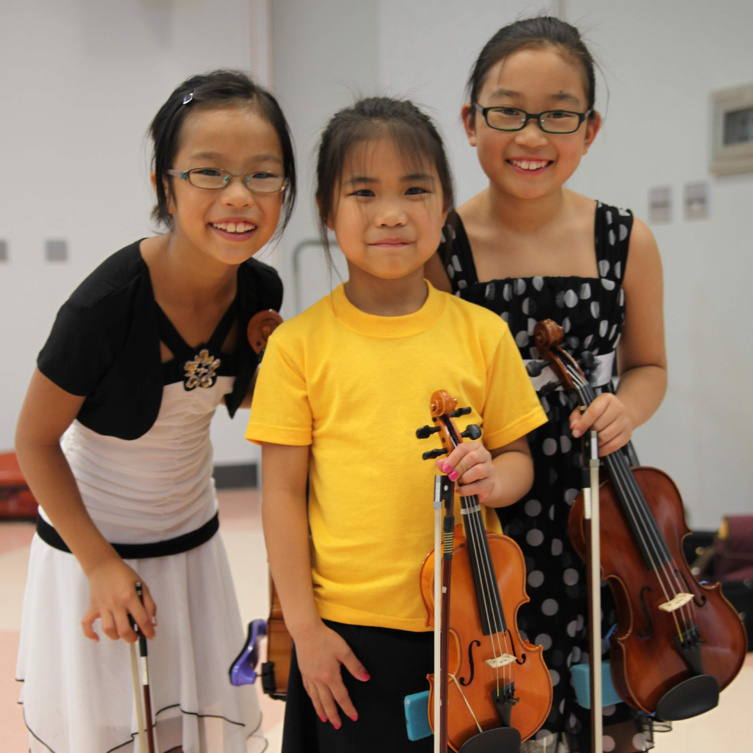 Three young students smile while holding string instruments