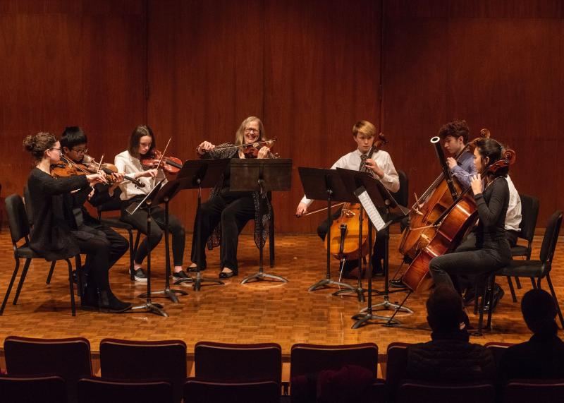 A Chamber Ensembles group and their instructor play string and wind instruments on stage.