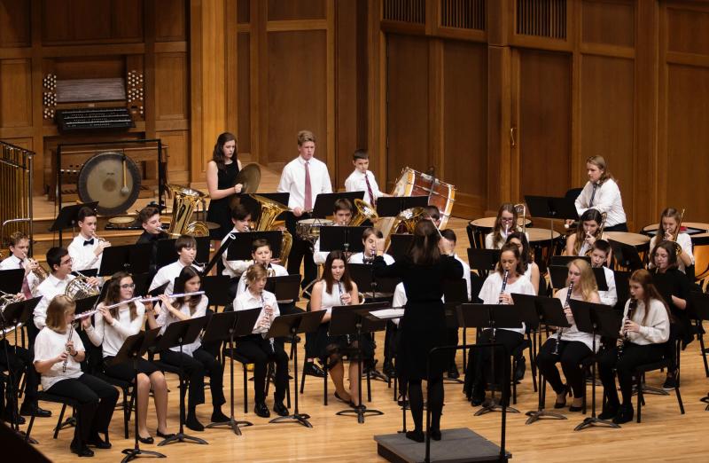 The Lawrence Community Symphonic Band performs onstage during a concert, their conductor in front.