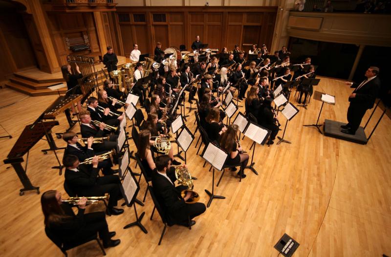 The Lawrence Community Wind Ensemble performs onstage during a concert, their teacher-conductor in front of them.