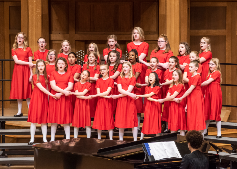 Allegretto choir holding hands performing on chapel stage in red dresses