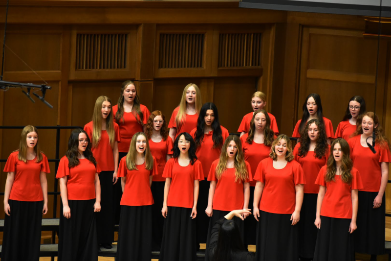 Arioso choir performing on chapel stage in red tops 