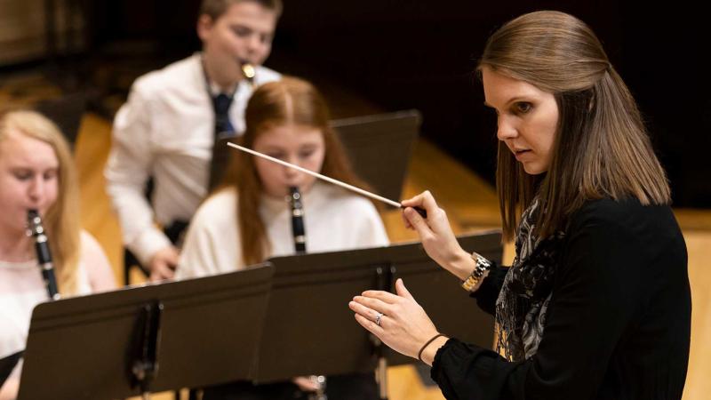 Teacher-conductor Caitlynn Acy holds a baton and directs the Lawrence Community Symphonic Band on the Chapel stage.