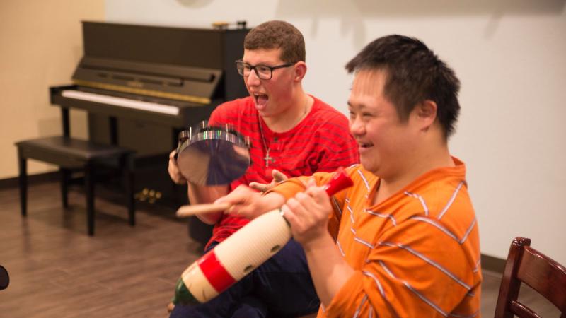 Two adult students play percussion instruments with wide smiles.