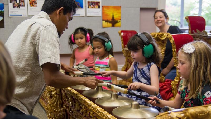 Instructor Dewa points at a Balinese metallophone while four young students play with mallets.