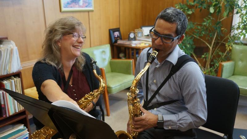 A teacher and student sit in a lesson with saxophones.