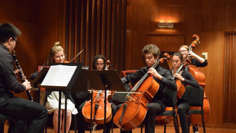 Six students play string and wind instruments onstage during a Chamber Ensembles recital.