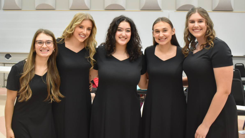 5 young ladies in black dresses smiling backstage