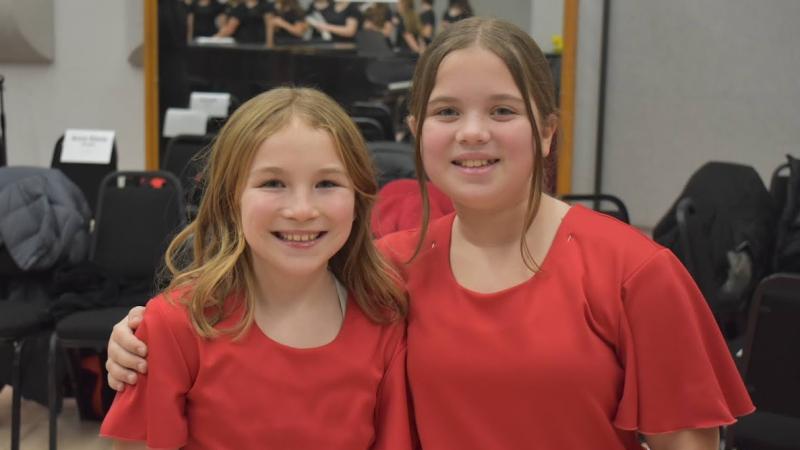 2 young singers in red tops smiling backstage