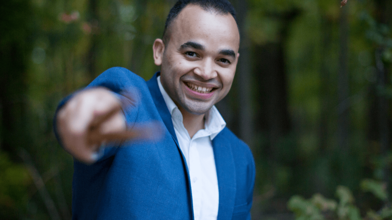 Man in blue blazer pointing with drum sticks